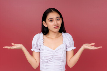 Portrait of a graceful Asian woman shrugging while presenting with open hands against a vibrant red backdrop, invoking choice and comparison.