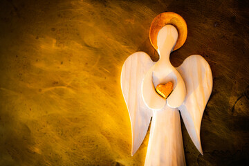 A wooden figure of an Angel with a golden halo. Golden heart. Burning background imitation. Grainy...