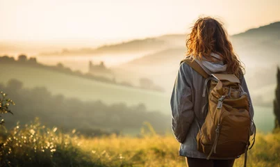 Gordijnen Female hiker traveling, walking alone Italian Tuscan Landscape view under sunset light. Woman traveler enjoys with backpack hiking in mountains. Travel, adventure, relax, recharge concept. © Andrii IURLOV