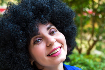 Portrait of woman with black curly hair and a beautiful smile in a blue dress.