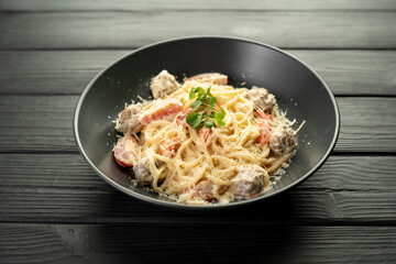Spaghetti with meatballs, creamy sauce, Parmesan cheese and tomatoes in a restaurant on a black plate on a dark background