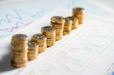 Stack of pound coins on financial graphs and figures - obrazy, fototapety, plakaty