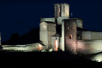 a medieval castle illuminated at night, highlighting its stone walls and towers against a dark sky