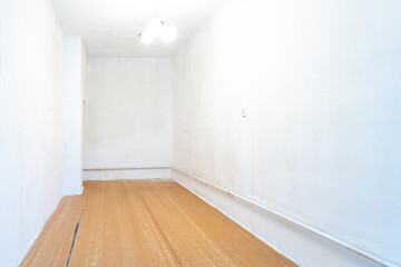 empty room with signs of wear, white walls that need repainting, an old wooden floor with visible damage, and a simple ceiling light fixture, suggesting a space ready for renovation or restoration