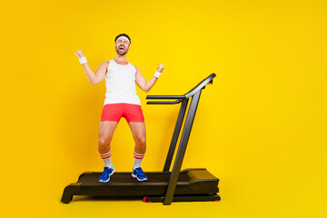 Full size portrait of ecstatic sporty guy stand treadmill raise fists accomplishment empty space...