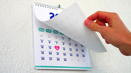 A male hand flipping a January page of the wall calendar 2024 showing the upcoming St Valentine's...