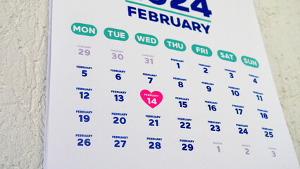 Close-up of St Valentine's Day date marking with a pink heart shape symbol on the wall calendar...