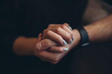 A gentle female hand with a ring on her finger holds a strong male hand. Low key. Dark, blurry background.