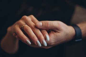 A strong male hand holds a gentle female hand with two gold rings on the finger. Low key. Dark, blurry background. - obrazy, fototapety, plakaty
