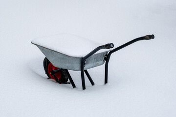 A metal wheelbarrow is covered with fluffy snow in a snowdrift