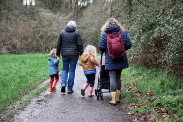 Liens familiaux sous la pluie, grand-mère, mère et deux enfants marchant de dos sur un chemin...