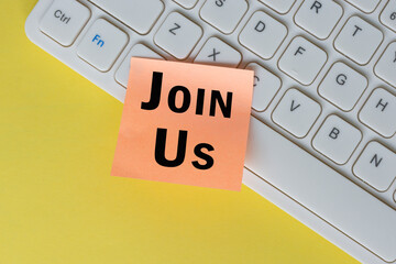 Join us text on orange sticky note on top of white keyboard.
