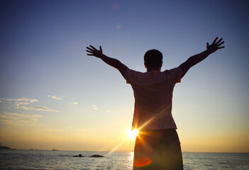 Silhouette of a man raising his hands or open arms on the beach at sunset