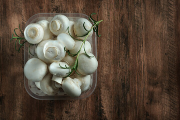 Fresh champignon mushrooms in a plastic box, top view, natural lighting with copy space