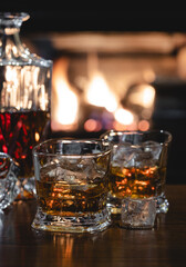Glasses of whiskey and decanter with burning fireplace in background