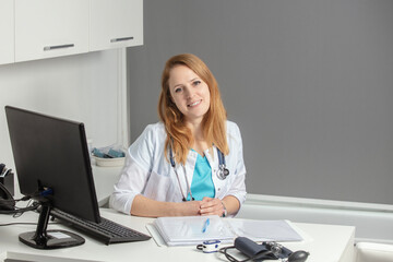 Portrait of young female medicine doctor sitting and working at her office. Healthcare and medical concept.Doctor in white coat doing paperwork at workplace with laptop, writing notes in the clinic. - obrazy, fototapety, plakaty