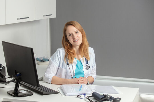 Portrait of young female medicine doctor sitting and working at her office. Healthcare and medical concept.Doctor in white coat doing paperwork at workplace with laptop, writing notes in the clinic.