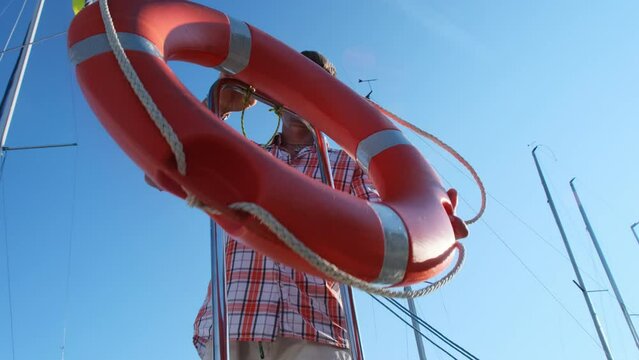 Marina worker fixes lifebuoy on metal construction in port. Professional man ensuring essential safety equipment readily accessible