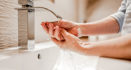Girl washing hands with soap foam in bathroom with steel faucet. Hygiene and cleaning procedure to...