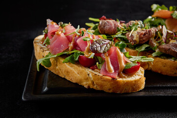 Bruschetta set with salmon, roast beef, and tuna on a black rectangular plate