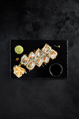 Top view of a Bonito roll with tuna flakes and salmon inside, served on a black slate with soy sauce, wasabi, and ginger