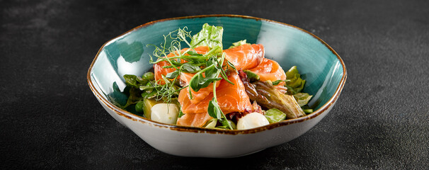 Salad with salmon, mozzarella, and avocado, served in a turquoise ceramic bowl