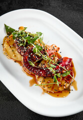 Grilled pineapple rings and tender octopus garnished with green herbs, served on a white elongated plate