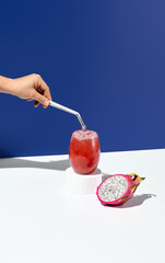 A hand stirring an exotic lemonade with dragon fruit, set on a white cylindrical display with a...