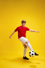 Obraz premium Young man in sportswear, uniform playing football, dribbling soccer ball against yellow studio background. Training. Concept of active lifestyle, youth, hobby and human emotions