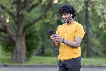 Fototapeta premium Active indian sportsman using smartphone while resting on park pathway