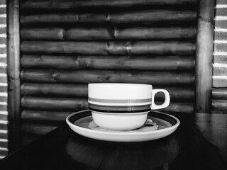 Black and white photo of coffee cup on the table with rustic decor in the background