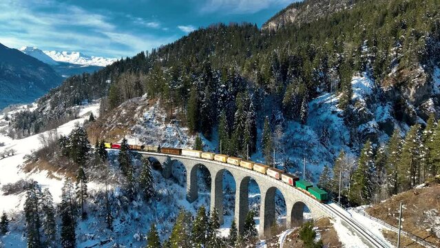 Aerial view of Landwasser Viaduct and Bernina express in Swiss Alps snow winter scenery. Drone shot red train passing through mountain in Filisur, Switzerland.