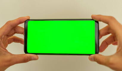 Female hands are holding smartphone with green screen mock up on neutral beige background Soft focus