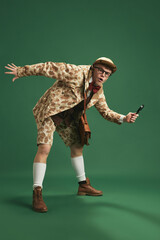 Young detective finding trail and investigating crime against green studio background. Profession...