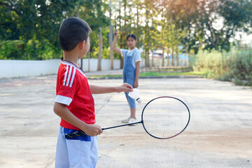 Asian girl and boy play badminton outdoors at the park together on vacation. Soft and selective...