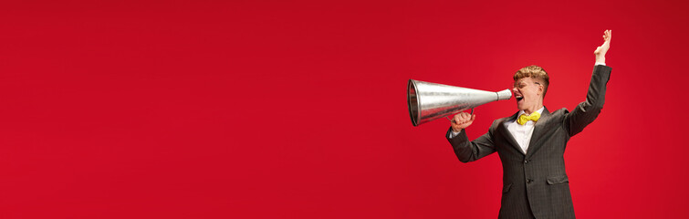 Announcement. Yong man in formalwear talking in megaphones against red studio background. Concept of business, youth, human emotions, lifestyle. Banner. Empty space to insert text, ad