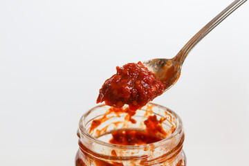 Sambal is an Indonesian chilli sauce or paste. On a silver spoon, taken from a transparent glass jar. Isolated on white background