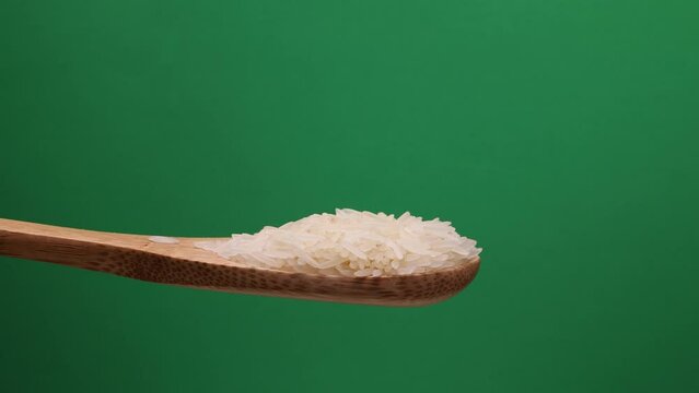 Uncooked raw white long grain rice pour drop fall on wooden spoon spin rotate pan green background