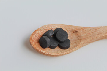 Fototapeta na wymiar Black tablets medicine on wooden spoon. Isolated on white background