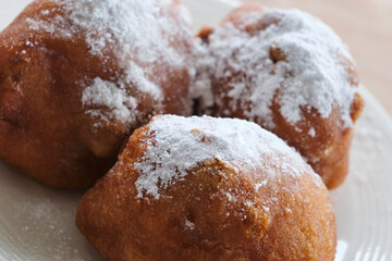 Typical dutch food commonly known as dutch doughnuts, dutchies or oliebollen with currants and powdered sugar on a white plate. Traditionally eaten on new year's eve in the Netherlands.	