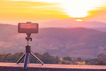 A smartphone is recording the sun setting over a mountain range. - Powered by Adobe