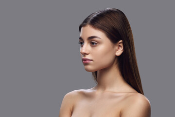 Side view portrait of young woman with clear skin, natural makeup, and neat hair against gray background. Concept of natural beauty and serenity, skin care products, nutritional supplements.