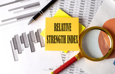 Relative Strength Index text on a sticky on the graph background with pen and magnifier