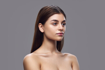 Fashion portrait of young woman with clear skin, natural makeup, and neat hair against gray background. Concept of natural beauty and serenity, skin care products, nutritional supplements.