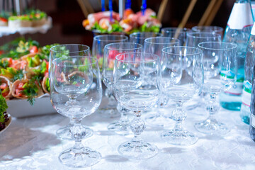A group of crystal wine glasses on a white tablecloth against the background of a festive table with appetizers with red fish, avocado and herbs