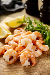 Cooked shrimps with lemon and rucola on wooden board.