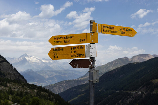 Walking trail directional signs at the famous Simplon Pass in Switzerland, with distance information and a background of mountains. Copy space above left.