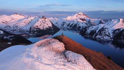 Tiny human standing in pink snow capped mountains over lake