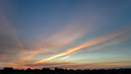 Beautiful evening sky at sunset over silhouettes of houses. Summer landscape.