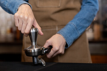 White Asian woman's hand Press the ground coffee tamper to make a close-up of espresso. Put on an apron